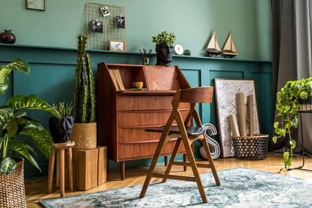 Modern and retro composition of home office interior with wooden cabinet, chair, plants, decoration...