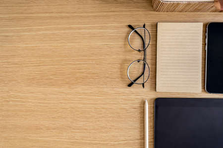 Stylish flat lay business composition on the wooden desk with glasses, notes, pen, copy space and office supplies in modern concept.の写真素材