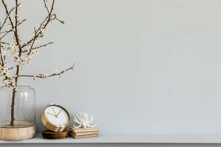 Minimalistic composition on the shelf with dried flower in design vase, gold clock, book and...