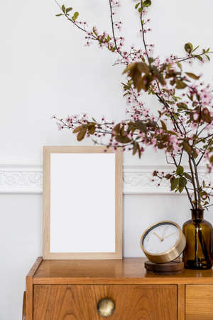 Stylish concept of home staging with mock up poster frame, design wooden commode, spring flowers,...