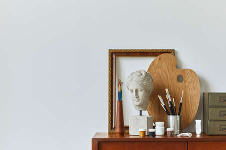 Stylish composition of artist workspace room with design retro teak commode, mock up poster frame, book, decoration and painting accessories. Template.の写真素材