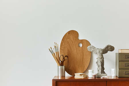 Stylish composition of artist workspace room with design retro teak commode, mock up poster frame, book, decoration and painting accessories. Template.の写真素材