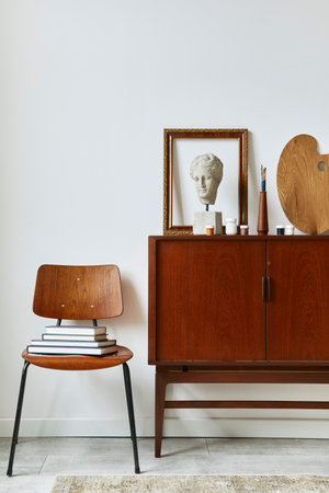 Stylish composition of artist workspace room with design retro teak commode, poster frames, easel, book, decoration and painting accessories. Template.の写真素材