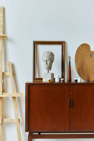 Stylish composition of artist workspace room with design retro teak commode, mock up poster frame, book, decoration and painting accessories. Template.の写真素材