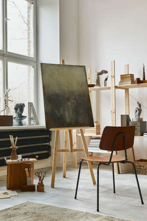 Unique artist workspace interior with stylish teak commode, wooden easel, bookcase, artworks, painting accessories, decoration and elegant personal stuff. Modern work room for artist. Template.の写真素材