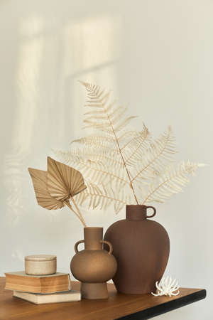 Stylish composition on the wooden table with design vases with dried flowers, book and decoration. Beautiful shadows on the wall. Abstract concept in modern interior. Template.の写真素材