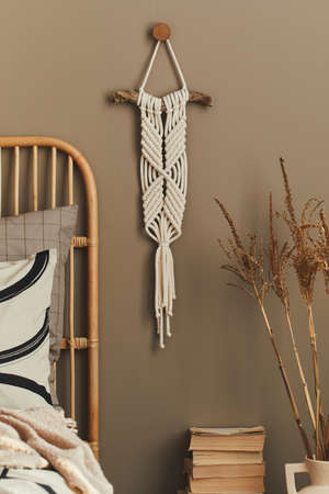 Cozy interior of stylish bedroom with design decoration, neutral macrame, dried flowers in vase, book, beautiful bed sheets, blanket, pillows and personal accessories. Template.の写真素材