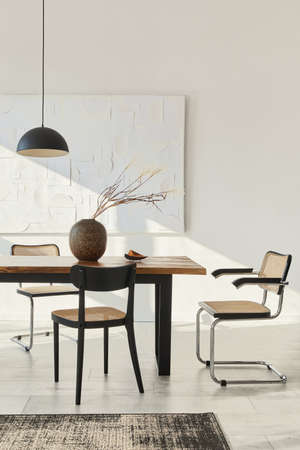 Minimalist composition of dining room interior with wooden table, design chairs, dried flowers in a...