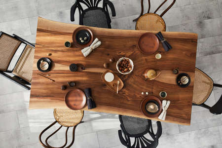 Stylish interior design of dining room with wooden walnut table, retro chairs, tableware, plates, tablecloth, teapot, food, decoration and elegant accessories. Cement floor. Template. Top view.の写真素材