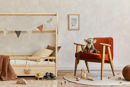 Stylish composition of cozy scandinavian child's room interior with wooden bed, red armchair, plush and wooden toys and hanging decorations. Neutral wall, carpet on the floor. Copy space. Template.の写真素材