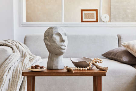 Creative composition of stylish and cozy living room decor with mock up poster frame, gray sofa, coffee table, sculpture and personal accessories. Beige neutral colors. Details. Template.の写真素材