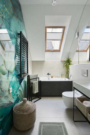 Stylish bathroom design with panels painted in green on the wall. Bathtub, towels, rattan baskets...