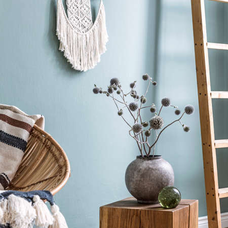 Stylish composition of living room interior with rattan armchair, design vase with dried flowers and...