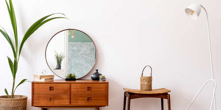 Minimalistic and stylish composition of living room with wooden commode, mirror, chair, lamp,...