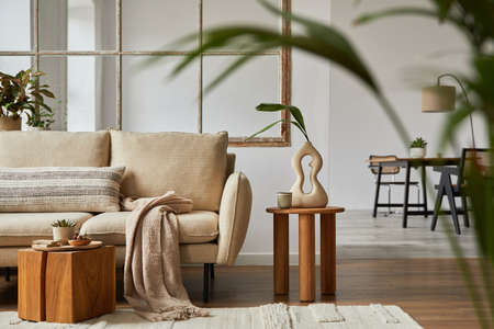 Modern living room interior design with beige sofa, wooden side table, plants and creative...