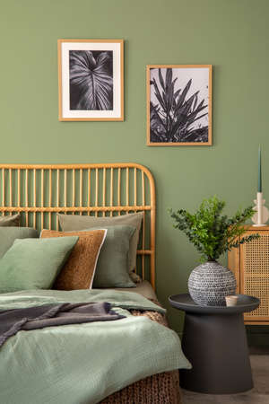 Stylish composition of modern bedroom interior. Mock up poster frames, rattan commode, bed and...
