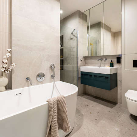 Modern bright bathroom interior with lamella wall. Big white bath with silver faucet and brown...