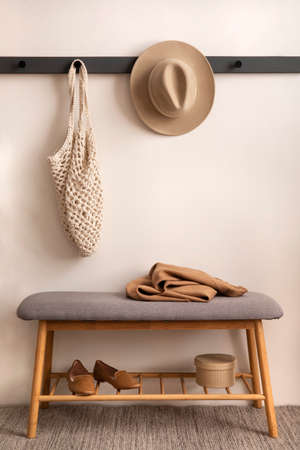The stylish composition of cozy entryway with wooden bench, coffee table, basket, hanger and personal accessories. Beige wall. Home decor. Template.の写真素材
