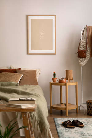 Stylish composition of cozy bedroom with mock up, beige bedding, plants, armchair and wooden coffee table. Mock up poster with wooden frame. Home decor. Template.の写真素材