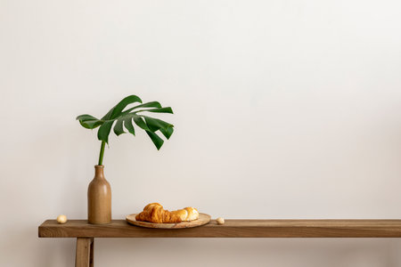 Interior design of simple living room with wooden bench, brown vase with green leaves, croissant on plate and personal accessories. home dÃ©cor. template.の写真素材