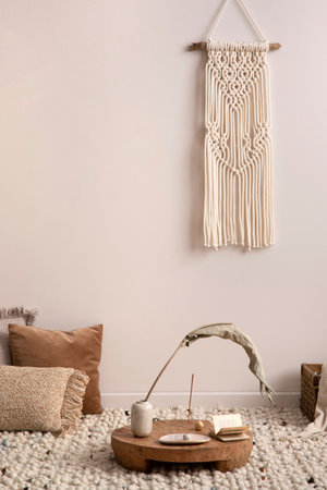 Cozy composition of meditation living room interior with beige carpet, pillows, macrame and personal...