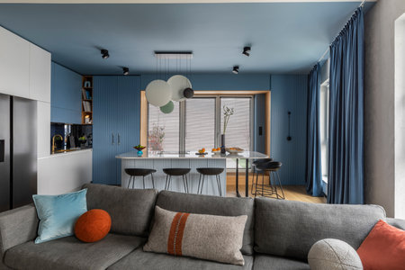 Interior design of kitchen interior with marble kitchen island, black chokers, blue kitchen furnitures, modern lamp, window, gray sofa, colorful pillows and personal accessories. home dÃ©cor. template.の写真素材