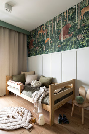 Creative composition of kids room interior with green forest wall paper, wooden bed, bottle green bedding, chair, simple gray curtain, rug and childrens accessories. home dÃ©cor. template.の写真素材