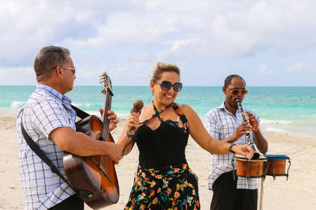 Trio ensemble of musicians consisting of two men and one woman performing on a sandy empty beach, Cuba, Varadero, 31 October 2016のeditorial素材