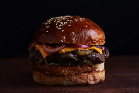 Burger against black background. with juicy meat, cheese and tomatoes, onionsの写真素材