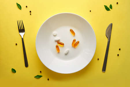 Pharmaceutical medicine pills or capsules on a plate with a fork and knife. Top view yellow background.の写真素材