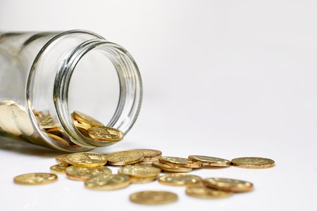 Collection of  coins spilling out of a glass jar tipped on its sideの写真素材