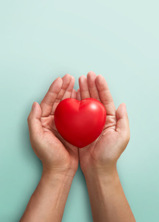 Adult hands holding red heart on light green backgroundの写真素材