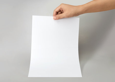 Hand holding a blank a4 size paper isolated on grey background.の写真素材