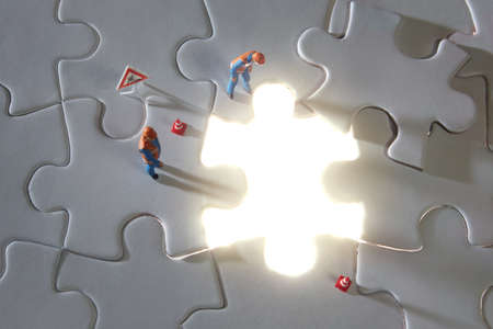 Miniature worker stand on white jigsaw puzzle with missed and shining piece. Solution concept.