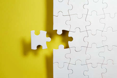Unfinished white jigsaw puzzle pieces on yellow backgroundの写真素材
