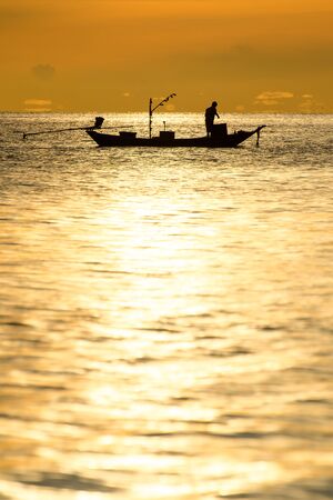 silhouette of fishermen in the boat on sea with yellow and orange sun in the backgroundの写真素材