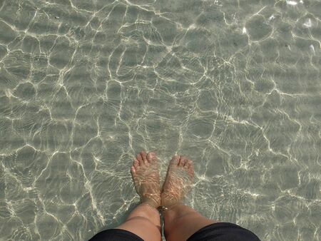 transparent water ripple, sand waves and sunlight glare. sea floor background with people leg and foot standの写真素材