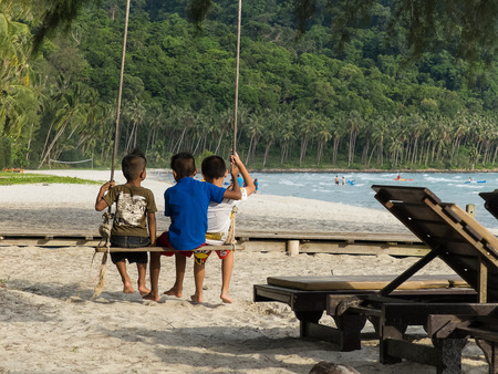 Little kids swinging with tropical beach on backgroundの写真素材