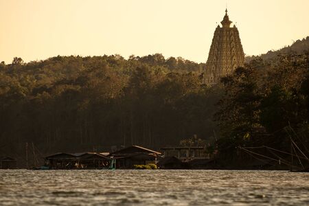 Silhouette golden chedi Buddhakhaya mon in the evening sunset sky with river and boat house at sangkhlaburi, thailandの写真素材