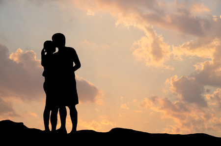 Silhouette of romantic a couple hug kissing against a sunset skyの写真素材