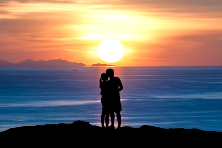 Silhouette of romantic a couple hug kissing against a sunset skyの写真素材