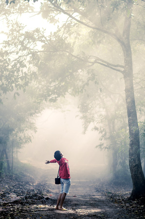 Man red shirt relax stand in the forest with the sunlight breaking through the trees. In the misty morning fog. (Oil Paint Filter)の写真素材