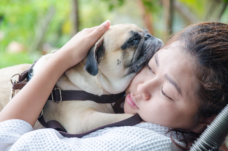 Teenage brunette girl playing hug and rest with her healthy young pug dog in the parkの写真素材
