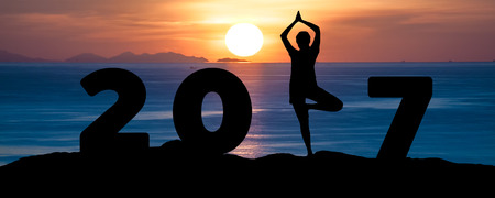 Silhouette young woman play Yoga on the sea and 2017 years while celebrating new yearの写真素材