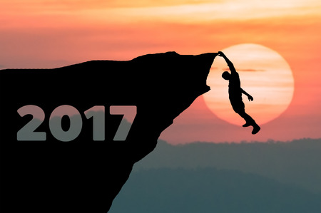 Silhouette Man climbs into cliff to the goal setting of word Happy New Year 2017 with sunset in background.の写真素材