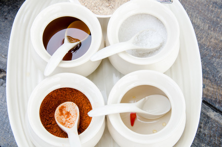 Unique Thai noodle garnish comprising sugar, fish sauce, vinegar and chili in white cup and tray on wood table in a restaurant served for lunch or dinnerの写真素材