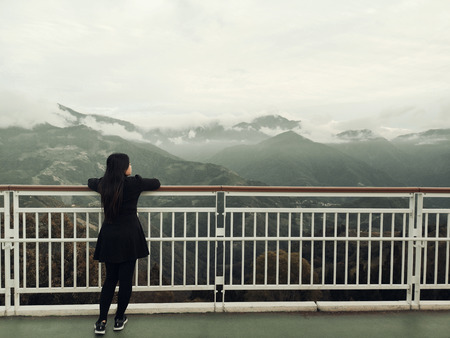Asian woman standing alone on balcony looking at white foggy and mountains backgroundの写真素材