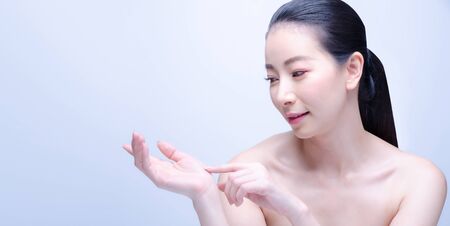 Beauty Spa Asian Woman with perfect skin Portrait. Beautiful Japanese Spa Girl showing empty copy space on the open hand palm for text. Proposing a product. Gestures for advertisement. Blue backgroundの写真素材