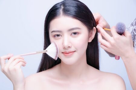 Makeup artist applies hair and skintone. Beautiful Asian woman face. Perfect makeup. Skincare foundationの写真素材