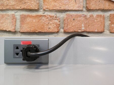 Black electric cord plugged into a metal grey socket in brick wall.